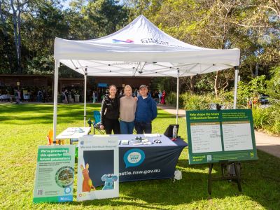 Three City of Newcastle staff standing under a marquee at Carnley Reserve with project signs around them, smiling at the camera